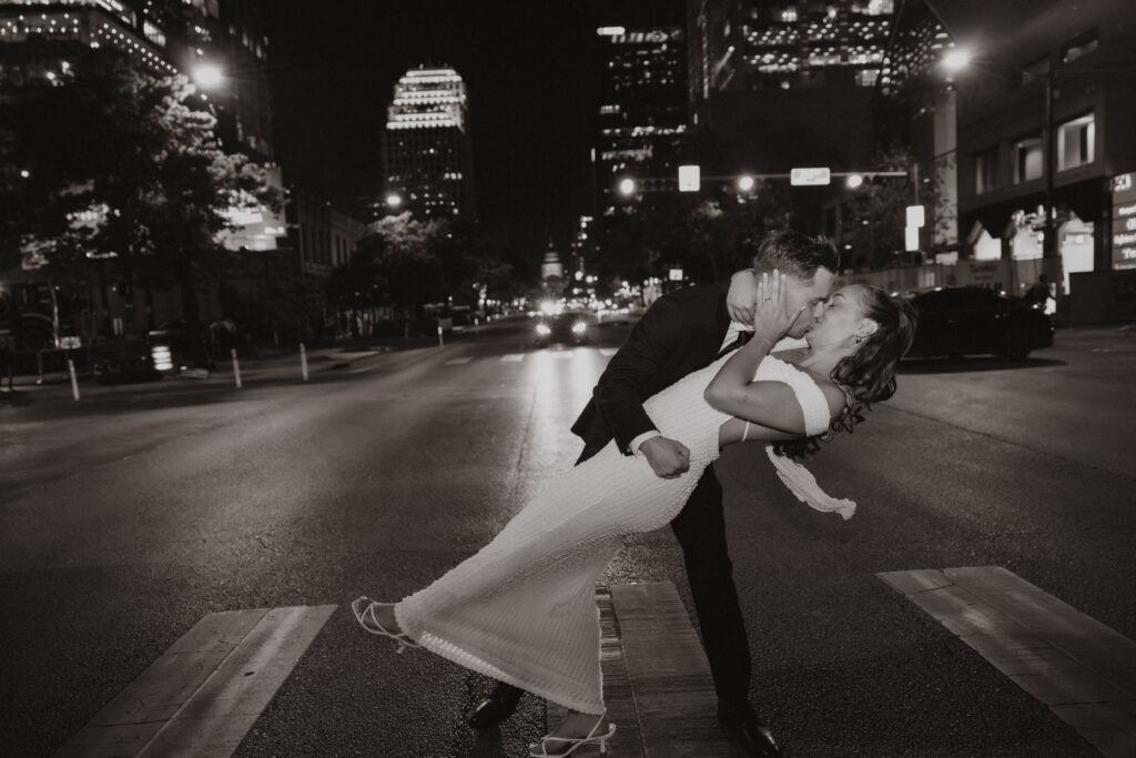 Couple walking hand in hand kissing at night with the Texas Capitol glowing in the background during their Austin engagement session
